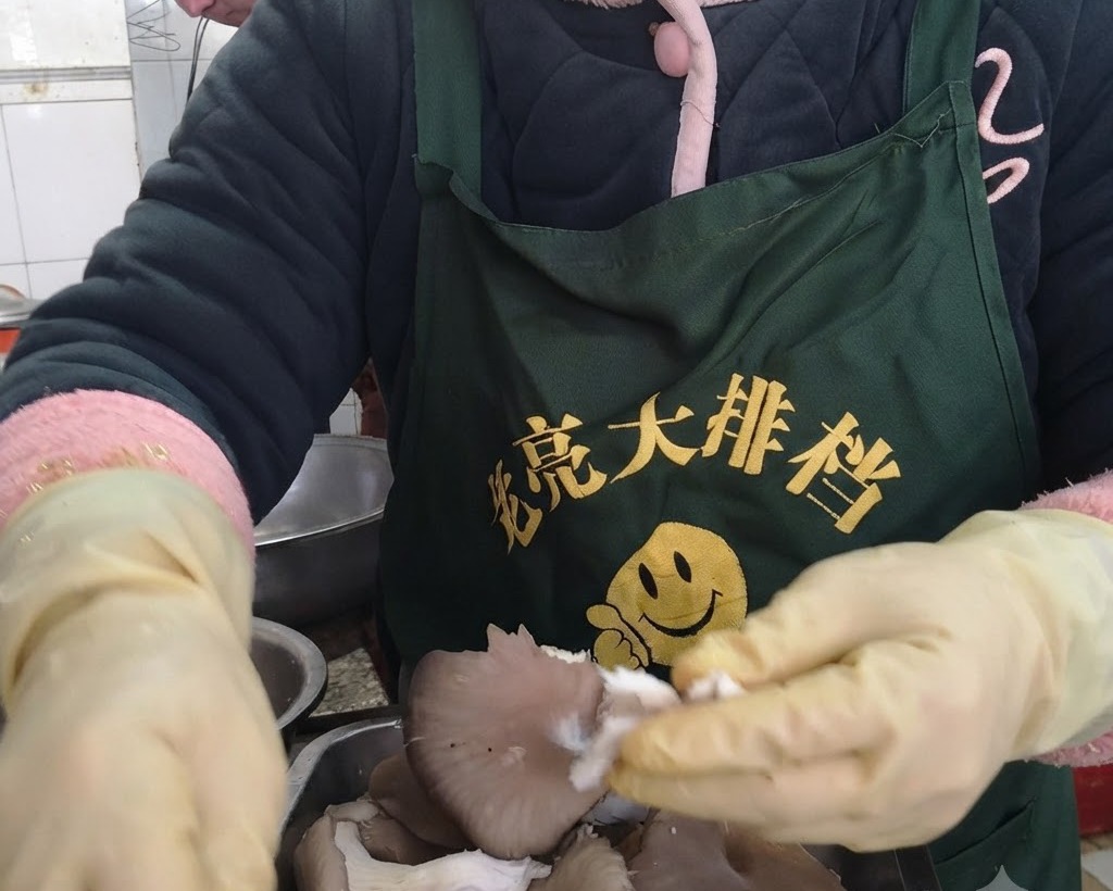 Manos con guantes protectores amarillos desgarrando champiñones ostra frescos en tiras individuales.
