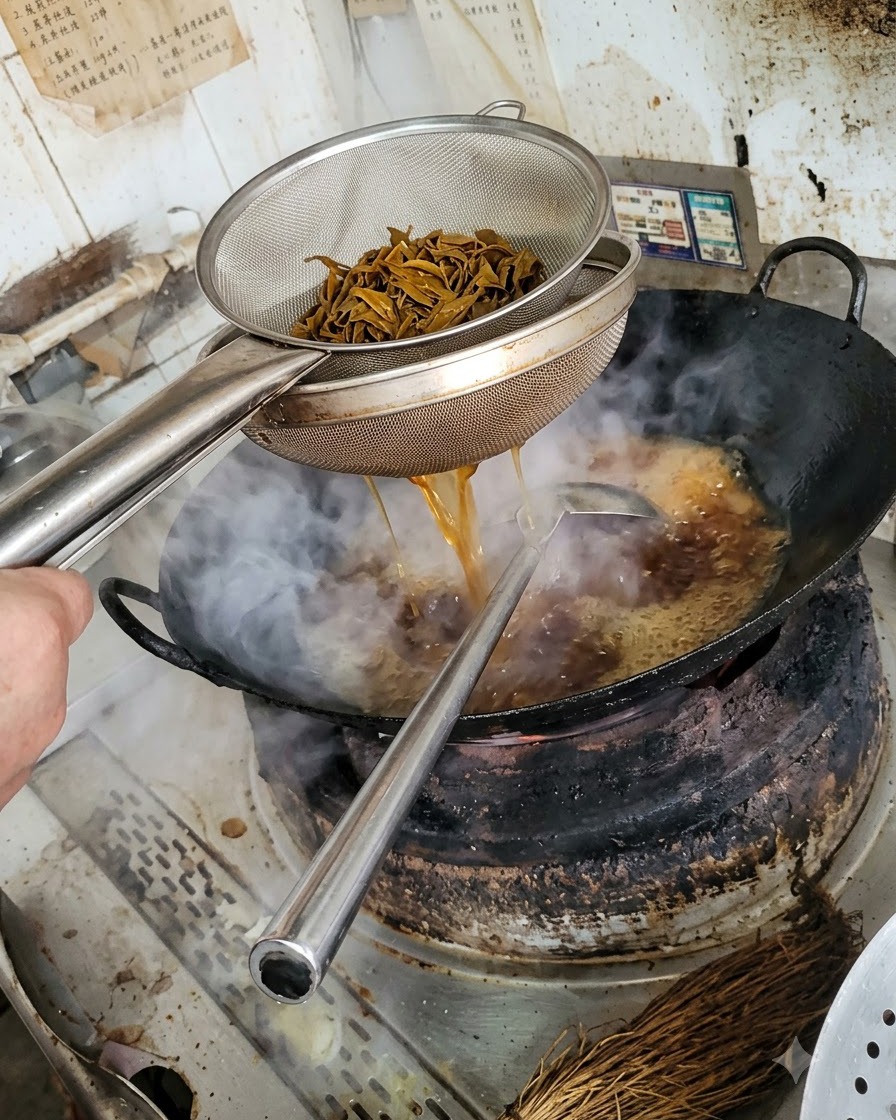 Un colador de metal con tiras de champiñón oscuras y escaldadas, mientras el líquido cae al wok de abajo.