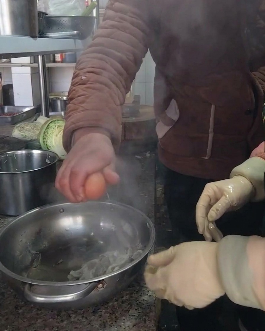 Una persona rompiendo un huevo marrón fresco en un bol de acero inoxidable con los champiñones preparados.