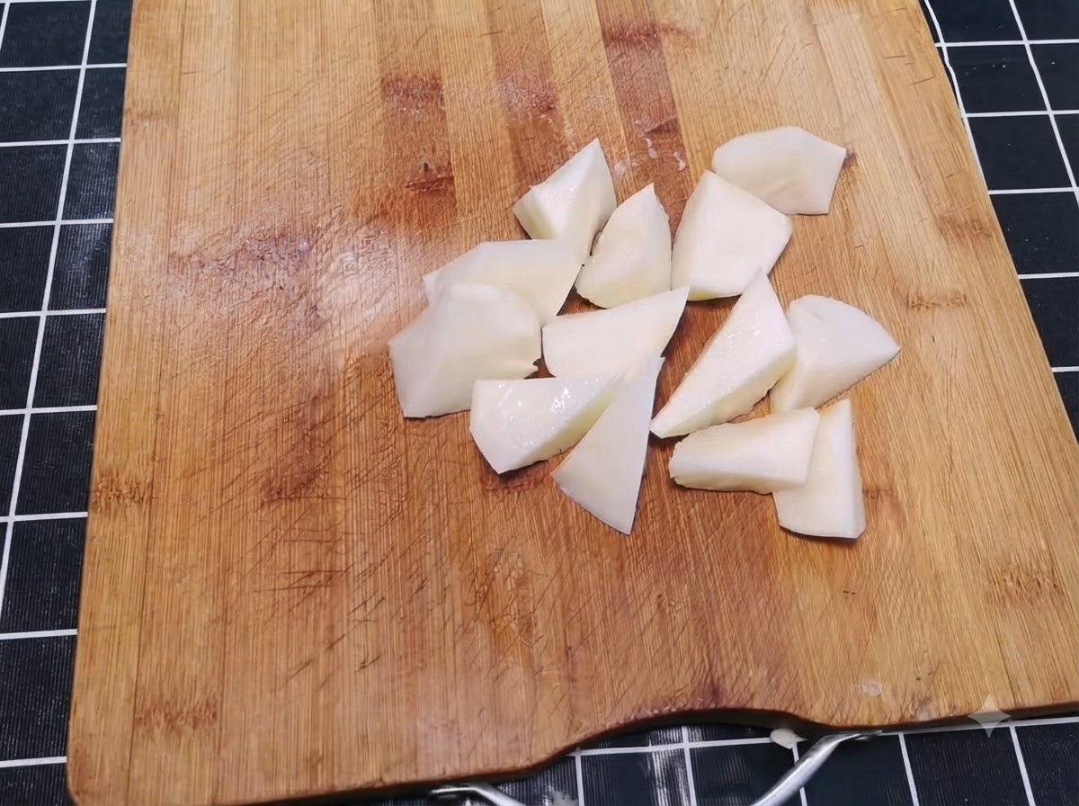 Patatas peladas cortadas en trozos irregulares del tamaño de un bocado esparcidas en una tabla de cortar de madera.