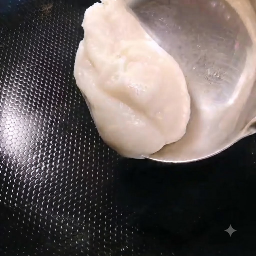Un cucharón añadiendo una porción de manteca de cerdo blanca en un wok negro caliente.