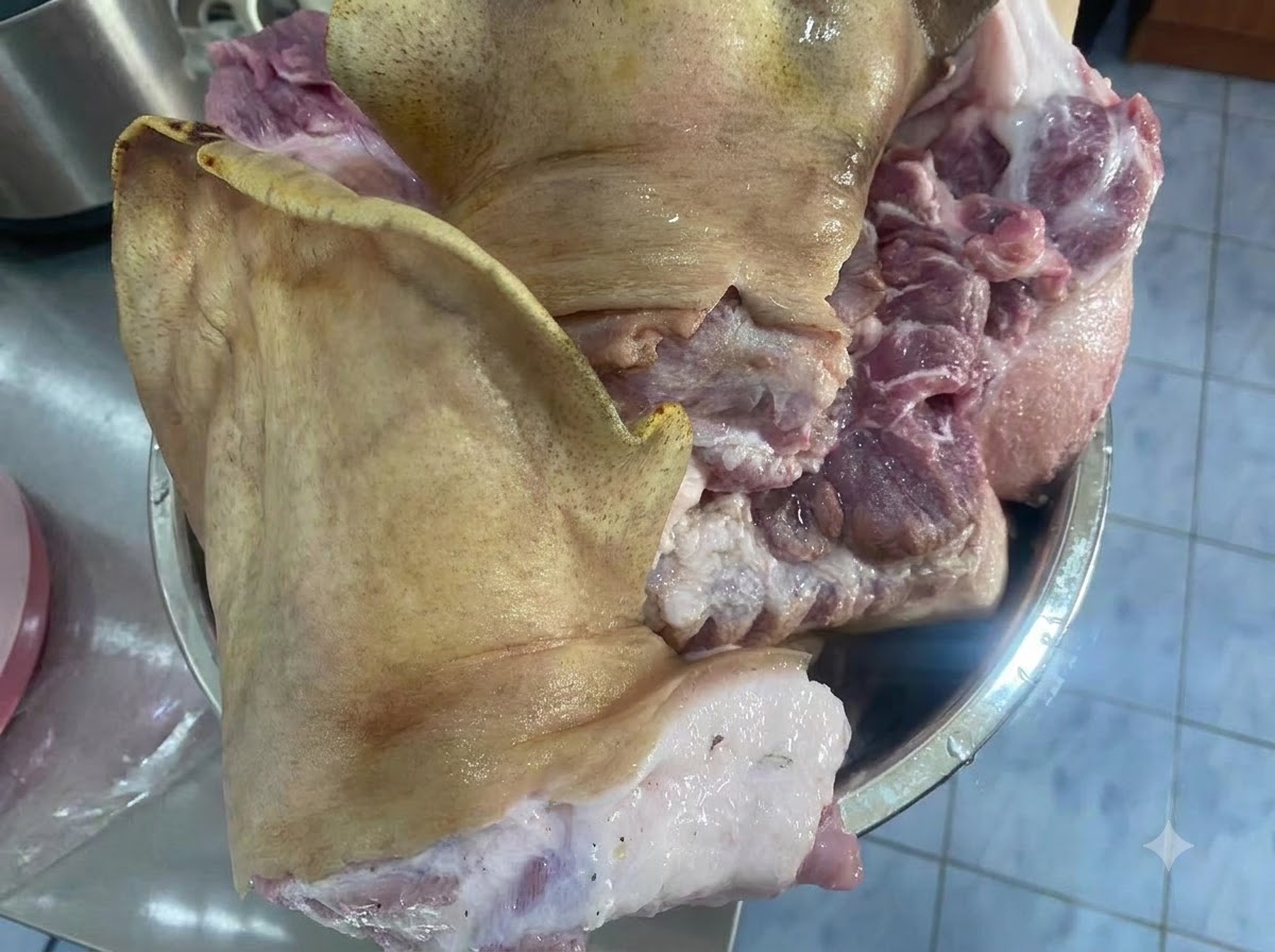 Grandes trozos crudos de una cara de cerdo reposando dentro de un bol metálico sobre una encimera.