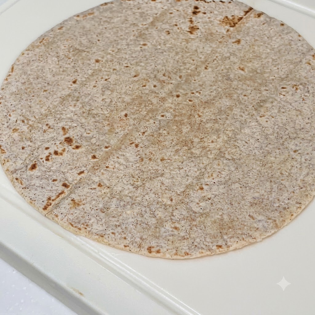 Una tortilla integral cubierta con salsa de mantequilla de maní, pollo en rodajas, repollo morado y lechuga fresca.