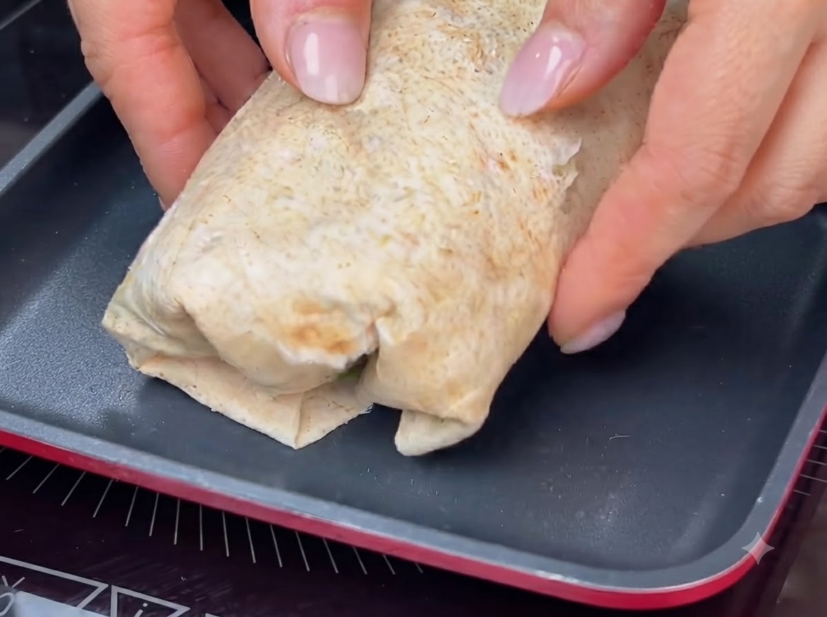 Un wrap enrollado siendo tostado en una sartén caliente para lograr una costra dorada.