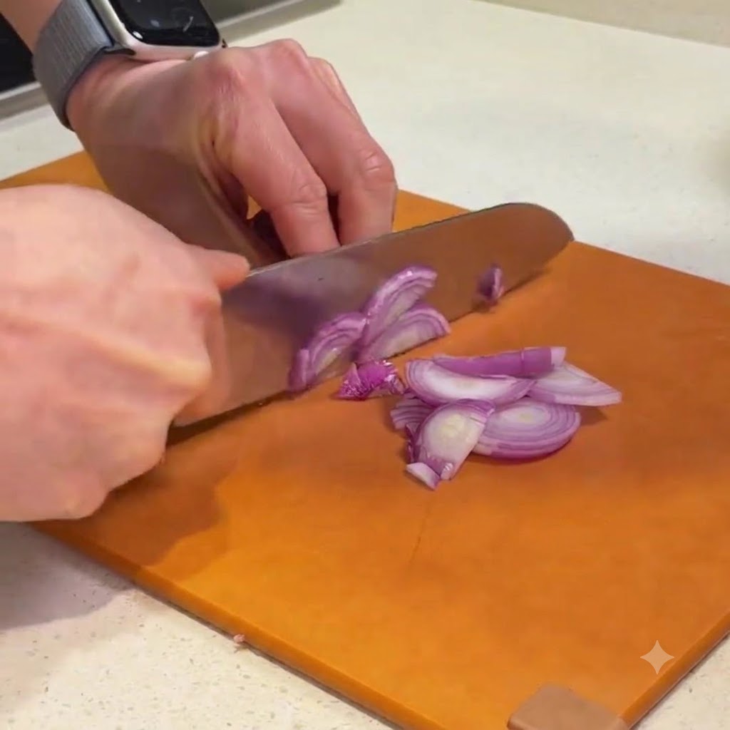 Chalotas rojas siendo cortadas en trozos finos sobre una tabla de cortar naranja.