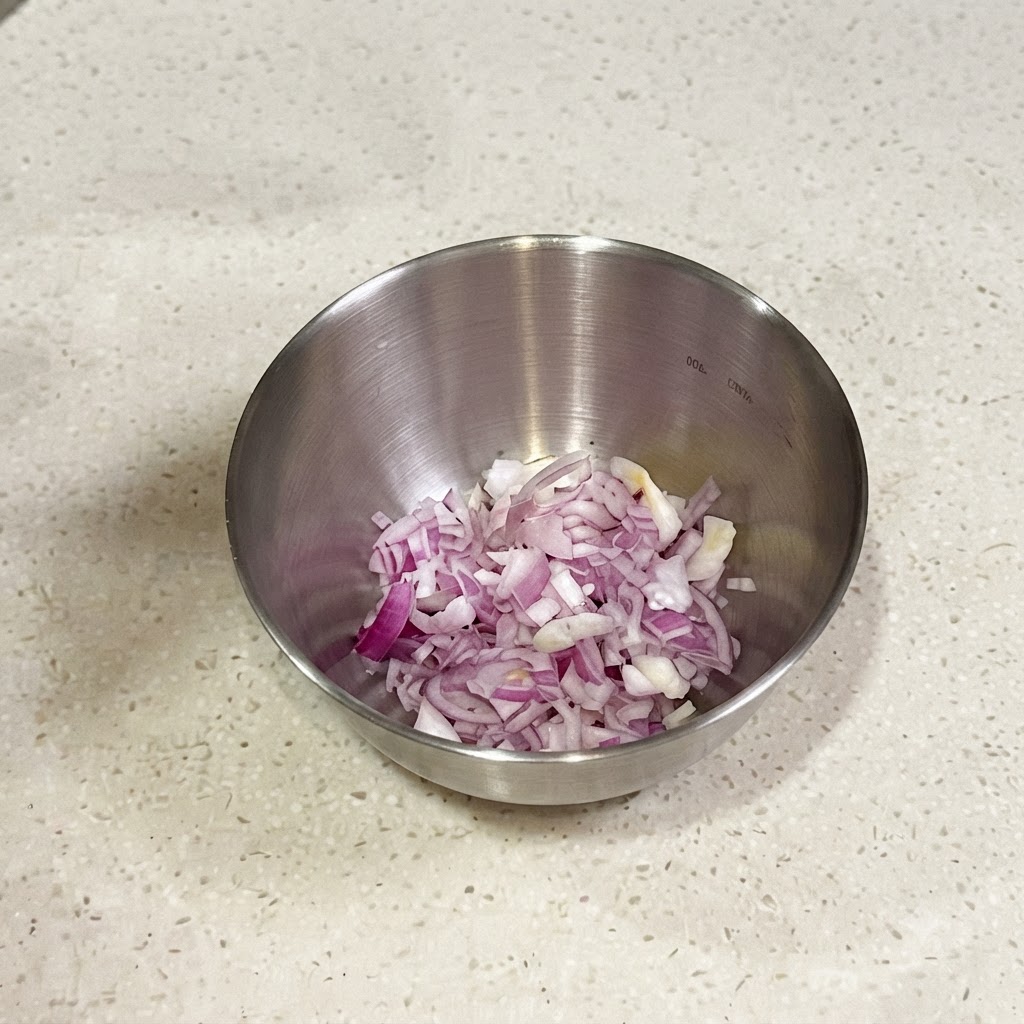Chalotas rojas y cebollinos finamente picados en un bol pequeño de metal listos para ser mezclados con condimentos.