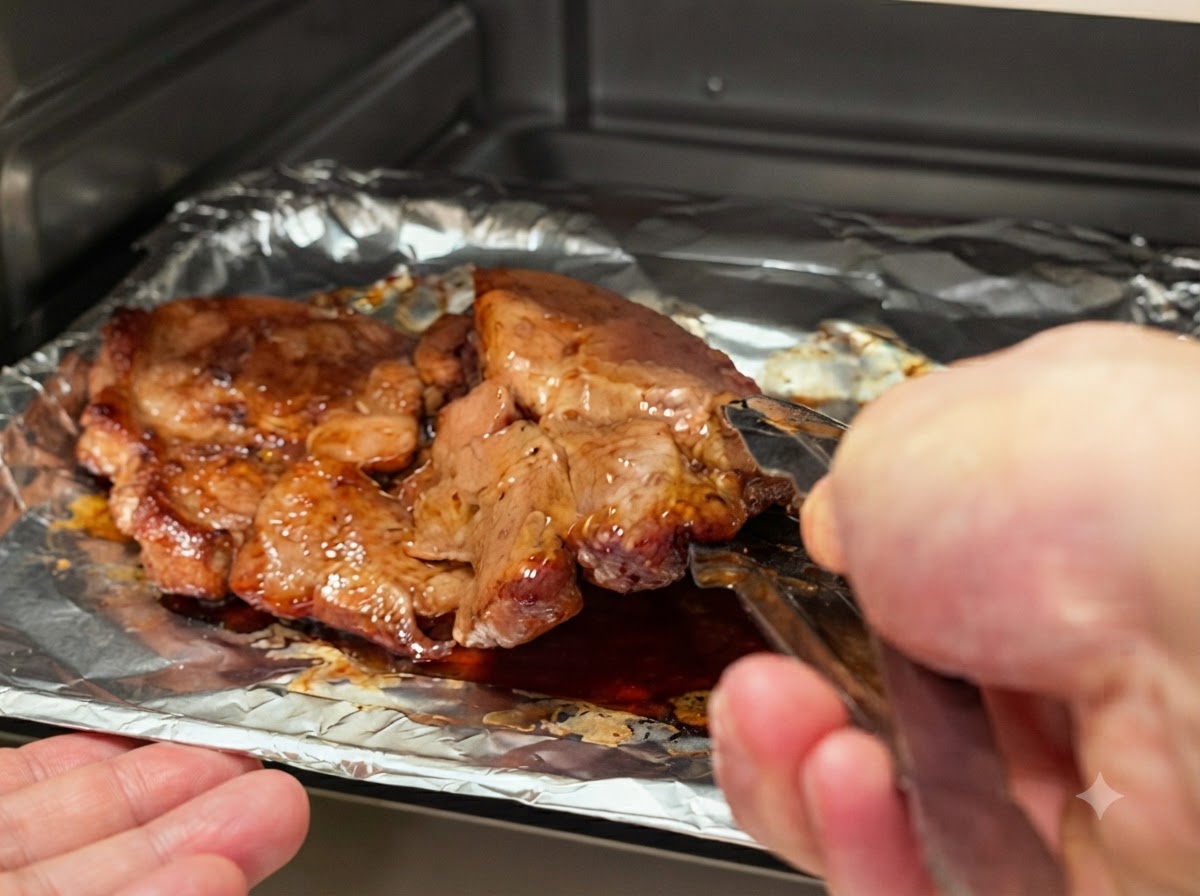 Chuletas de cerdo siendo volteadas en la bandeja de horno usando pinzas de cocina de metal.