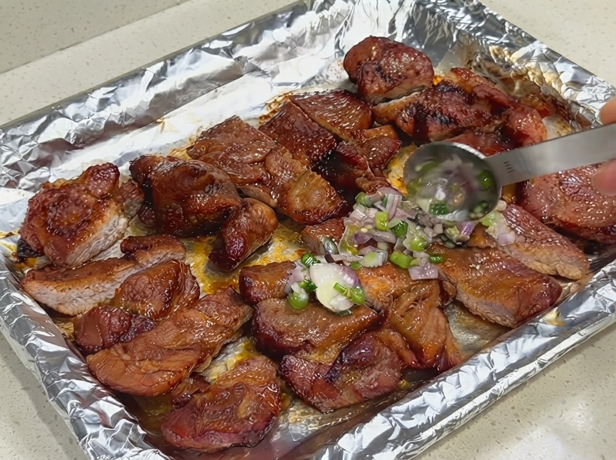Cuchara aplicando una capa de salsa fresca de cebollino y chalota sobre cerdo cortado en una bandeja de horno forrada de papel aluminio.