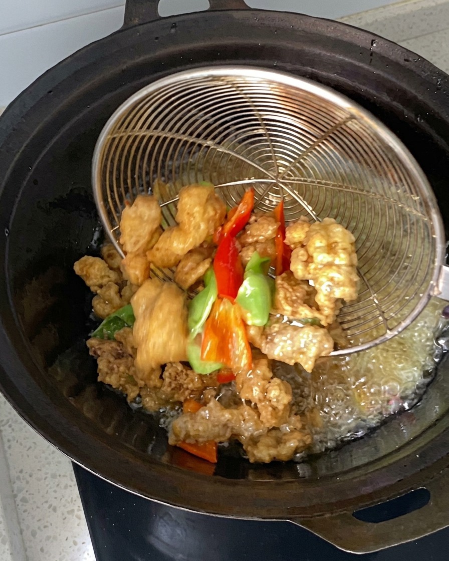 Trozos de carne marinada y pimiento siendo sumergidos y recogidos con un colador de alambre en un wok con aceite caliente.