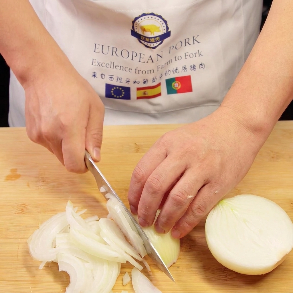 Las manos de un chef cortando una cebolla en tiras finas sobre una tabla de cortar de madera.