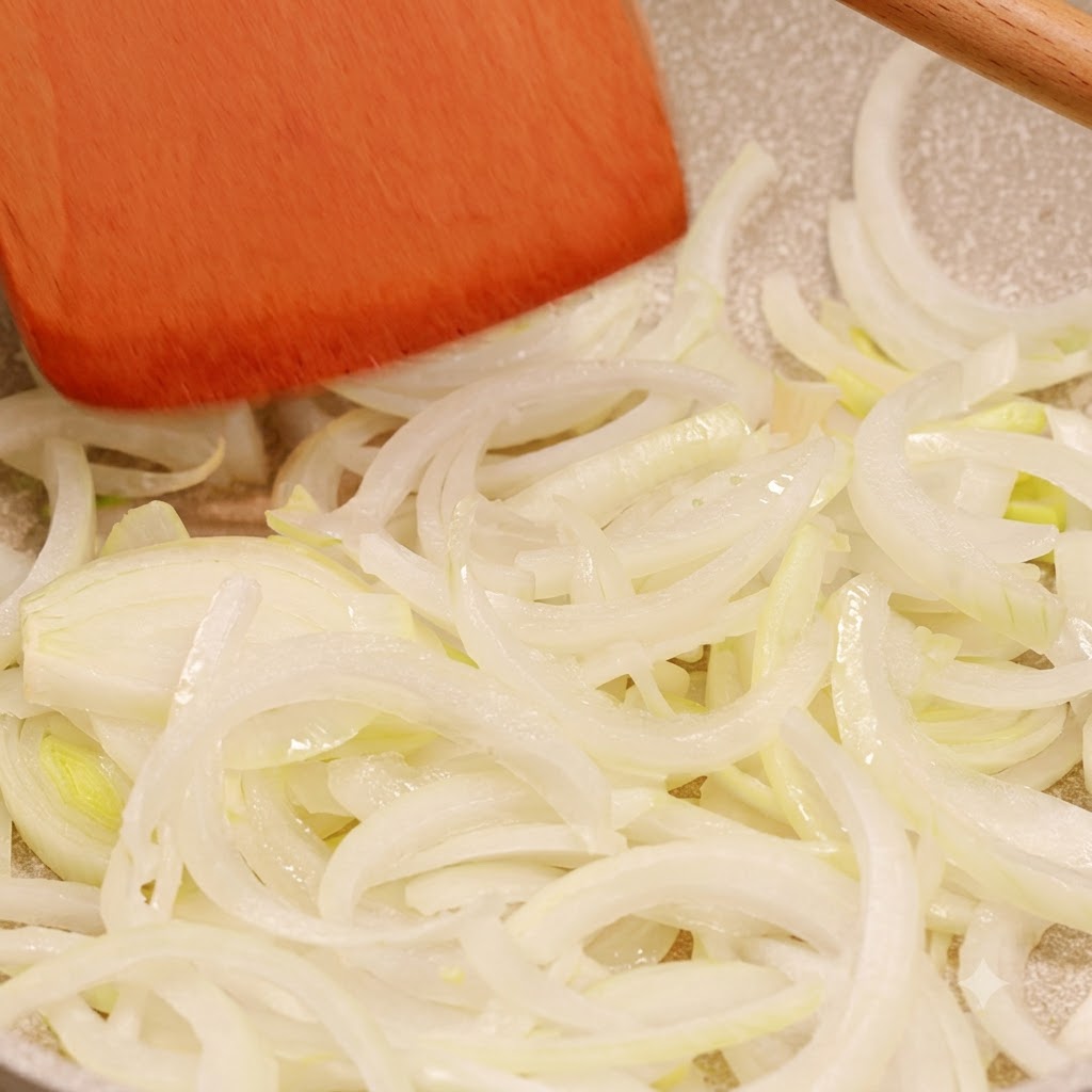 Cebollas en tiras cocinándose en una sartén siendo movidas con una espátula de madera.