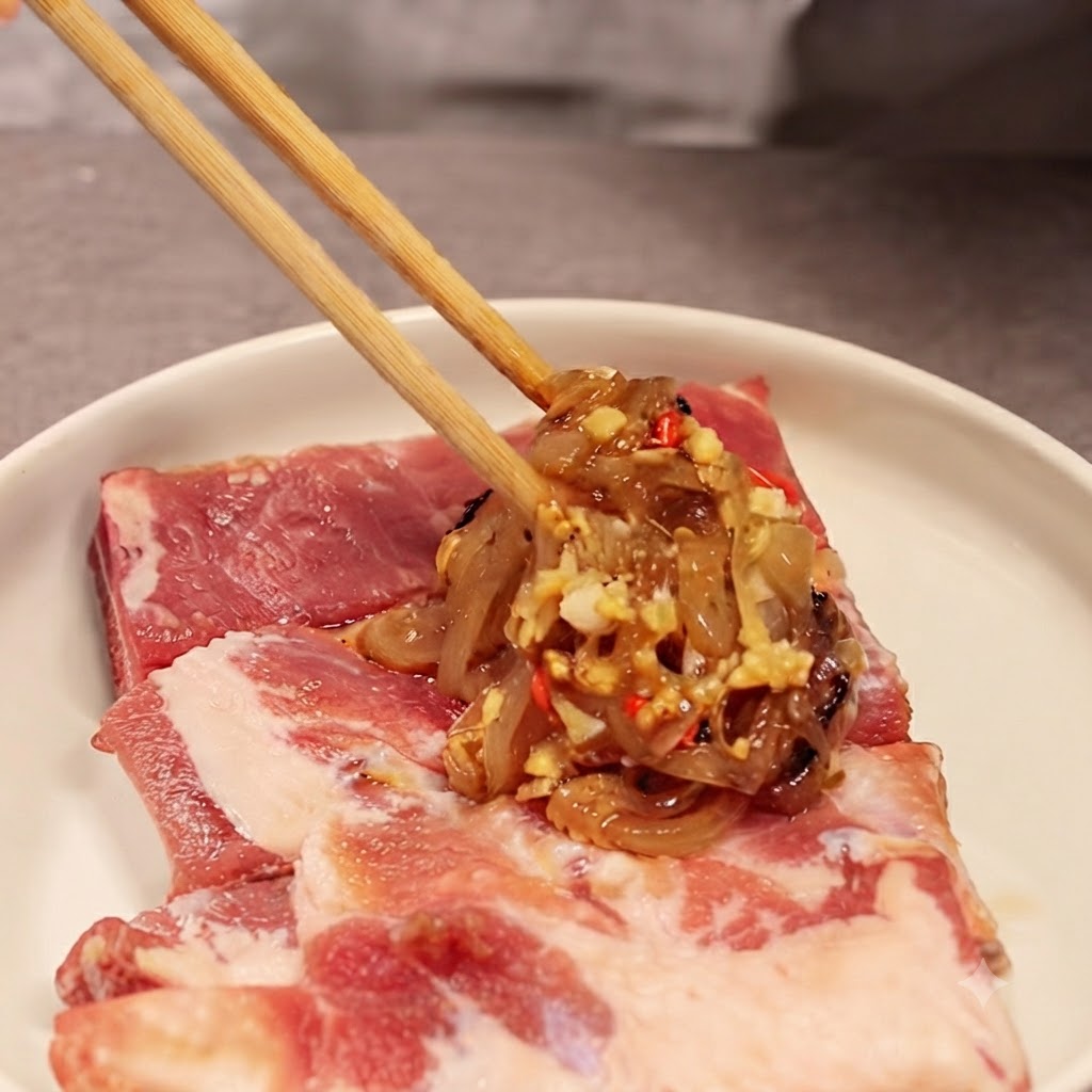 Palillos sosteniendo una porción de la mezcla de cebolla y salsa sobre costillas de cerdo crudas en un plato blanco.