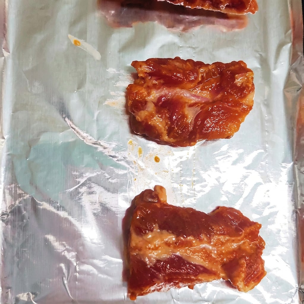 Trozos de costilla de cerdo marinada dispuestos ordenadamente en una sola fila sobre una bandeja de horno forrada con papel de aluminio.