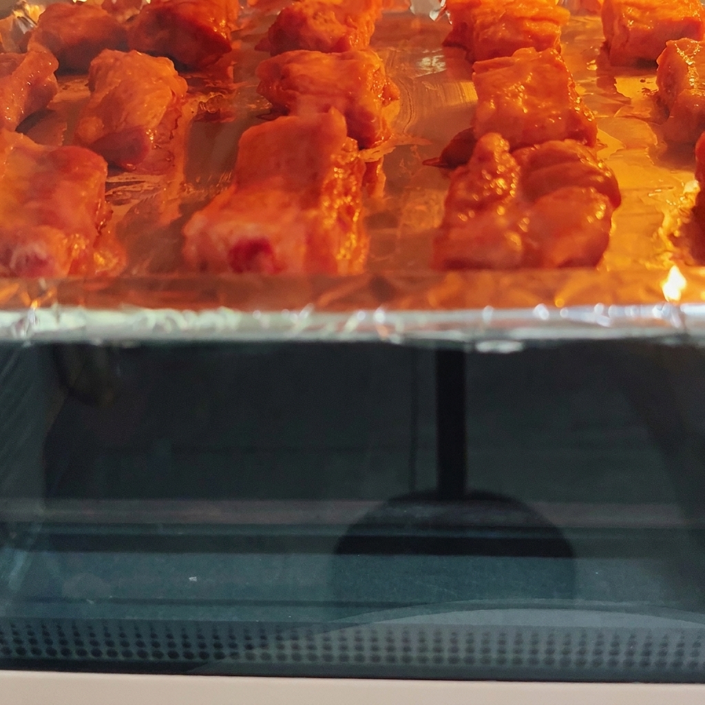 Costillas de cerdo asándose dentro de un horno caliente en una bandeja, mostrando un dorado visible bajo el elemento calefactor.
