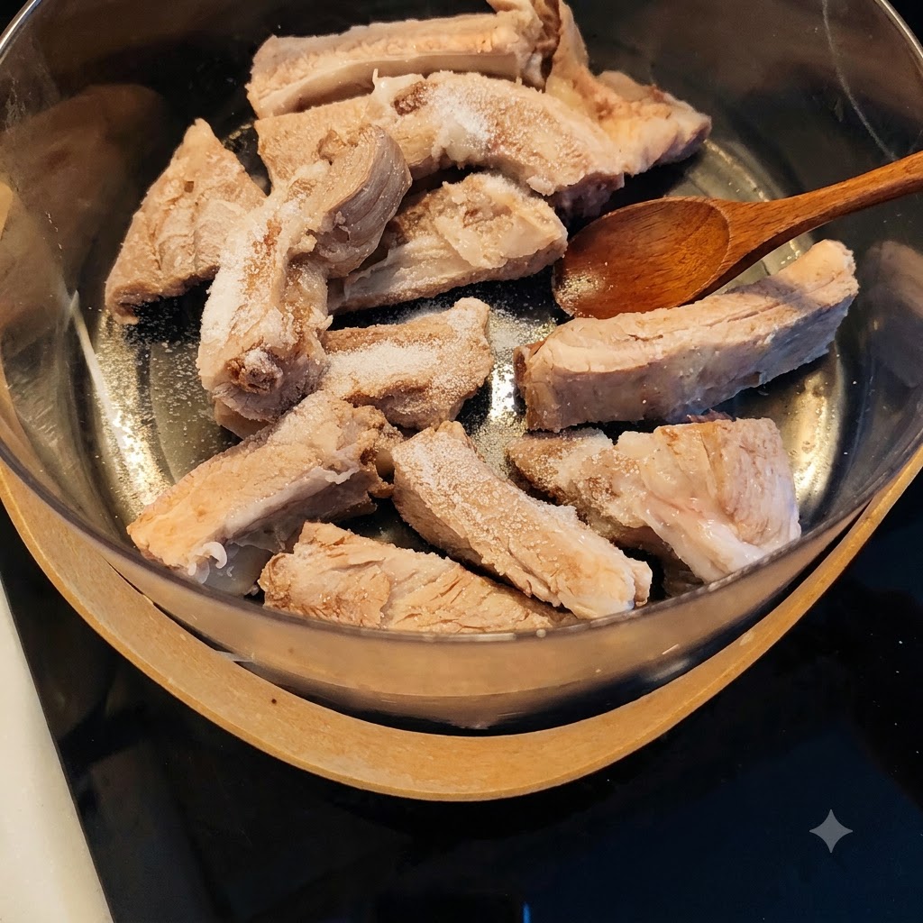 Una cuchara de madera sobre costillas de cerdo escaldadas espolvoreadas con sal y condimentos dentro de una olla.