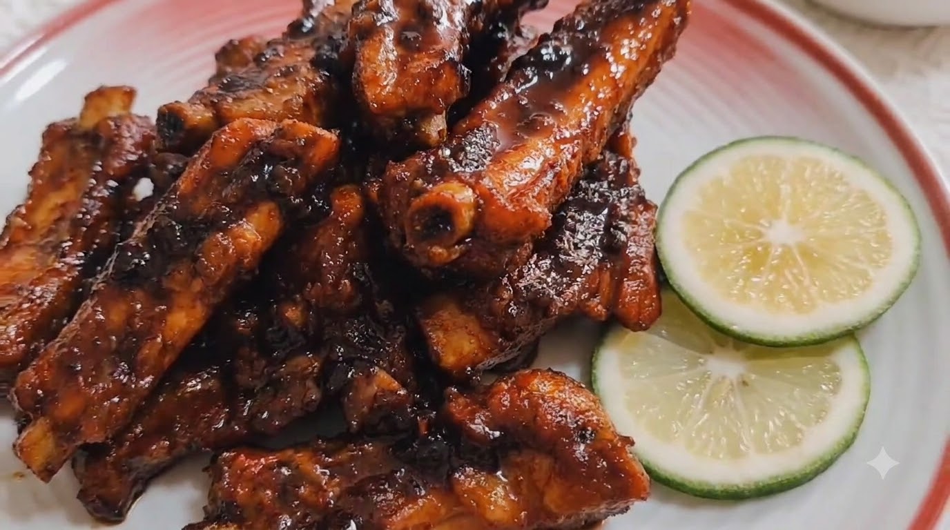 Costillas de cerdo braseadas al café servidas en un plato de cerámica con borde rojo y decoradas con rodajas de lima.
