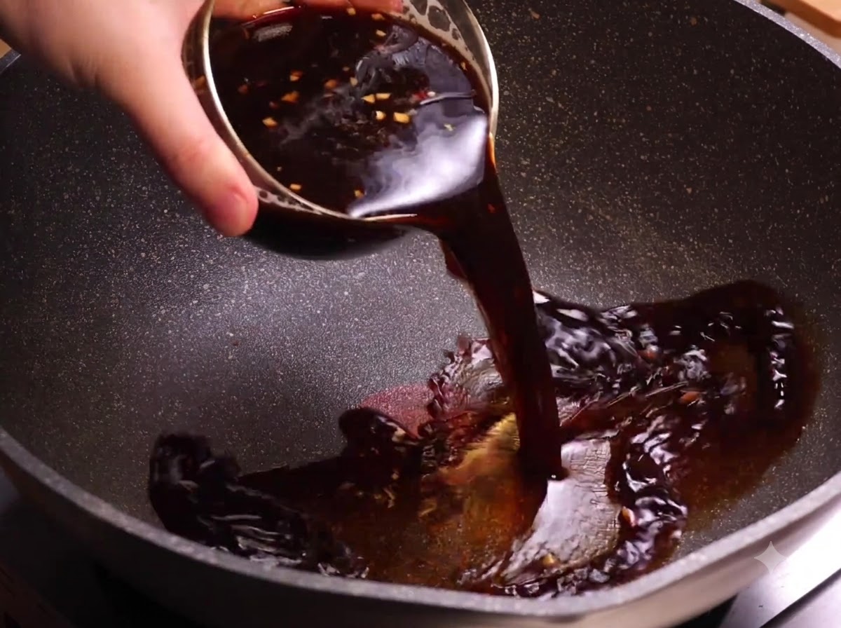 Un bol de salsa de café oscura siendo vertido en un wok caliente.