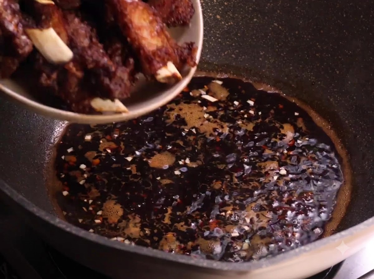 Costillas de cerdo fritas siendo transferidas desde un plato a la salsa oscura que hierve a fuego lento en un wok.
