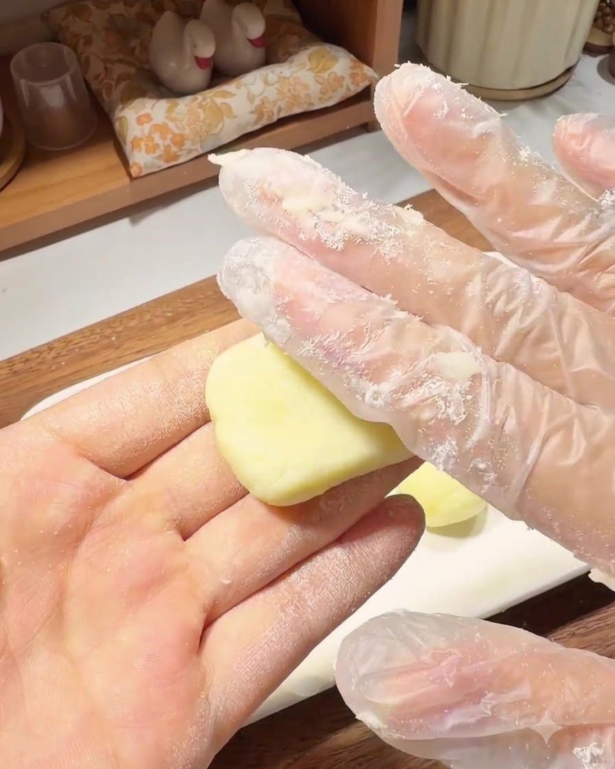 Una mano enguantada presionando una pequeña bola de masa de patata para darle forma de tortita redonda y plana en la palma de la mano.