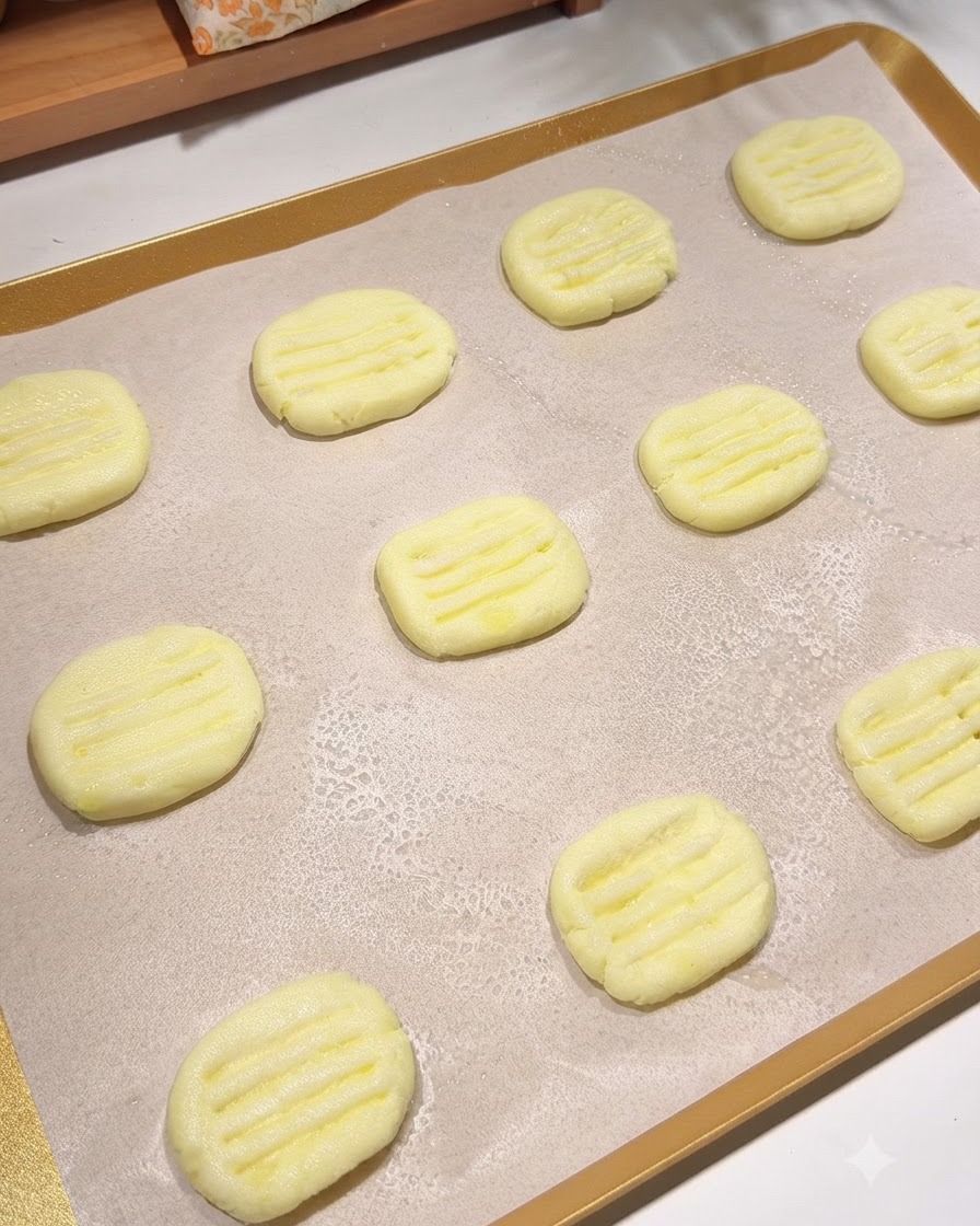 Una bandeja para hornear forrada con papel pergamino que sostiene múltiples tortitas de patata moldeadas con una fina capa de aceite de cocina pulverizado sobre ellas.
