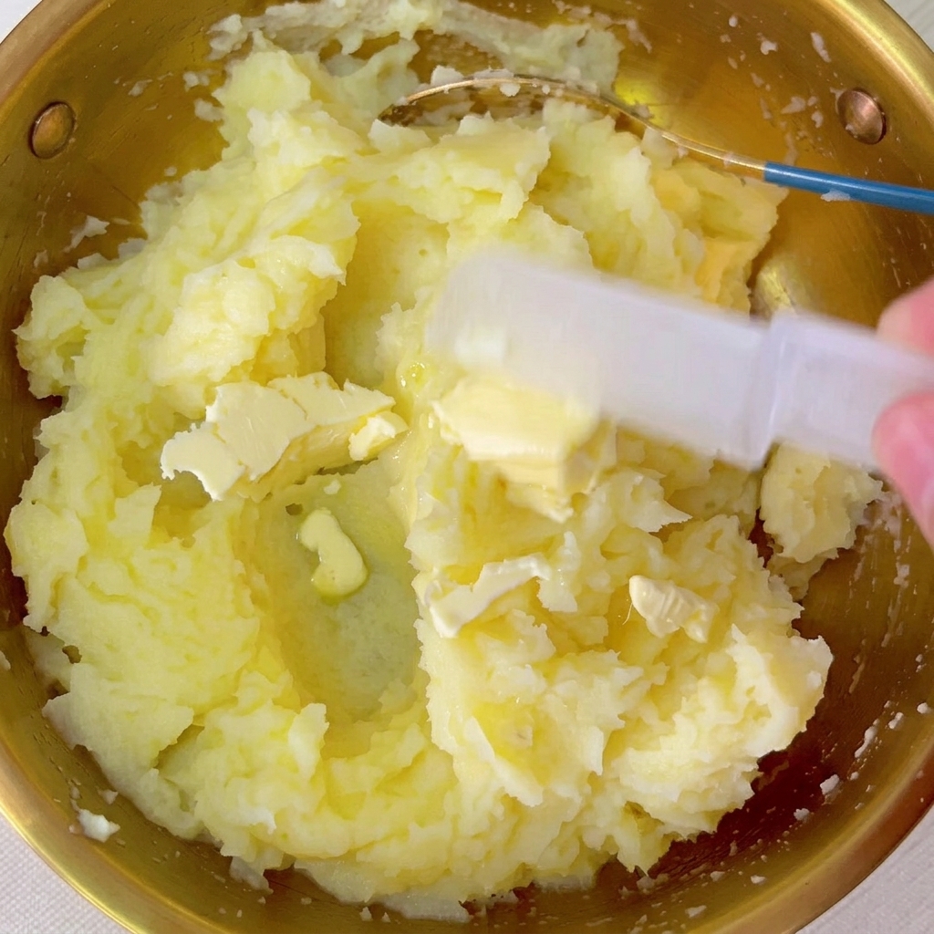 Trozo de mantequilla siendo mezclado en el cuenco de puré de papa tibio.