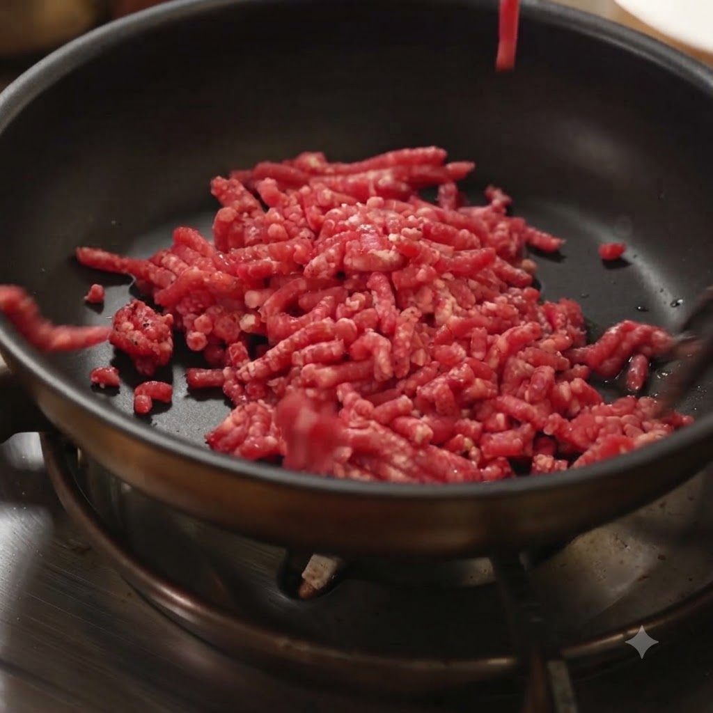 Carne picada cruda siendo añadida a una sartén negra caliente sobre un fogón.