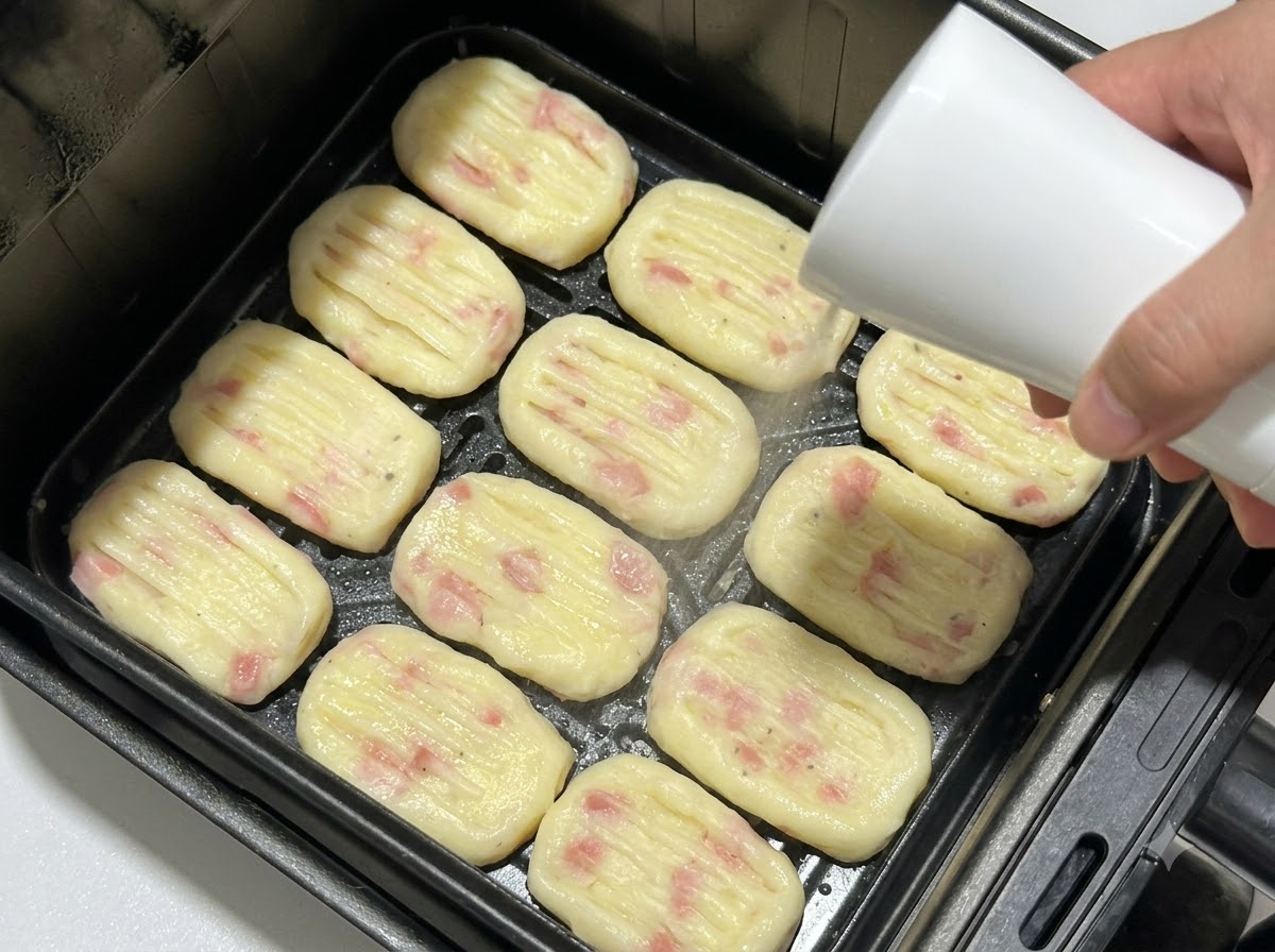 Tortitas de patata con forma colocadas en la cesta de la freidora de aire mientras son pulverizadas con aceite desde una botella de spray.