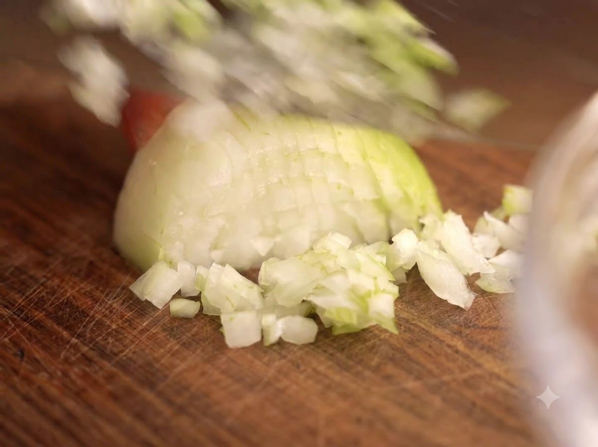 Un cuchillo picando cebollas y ajo en una tabla de madera junto a un bol de vidrio con carne.