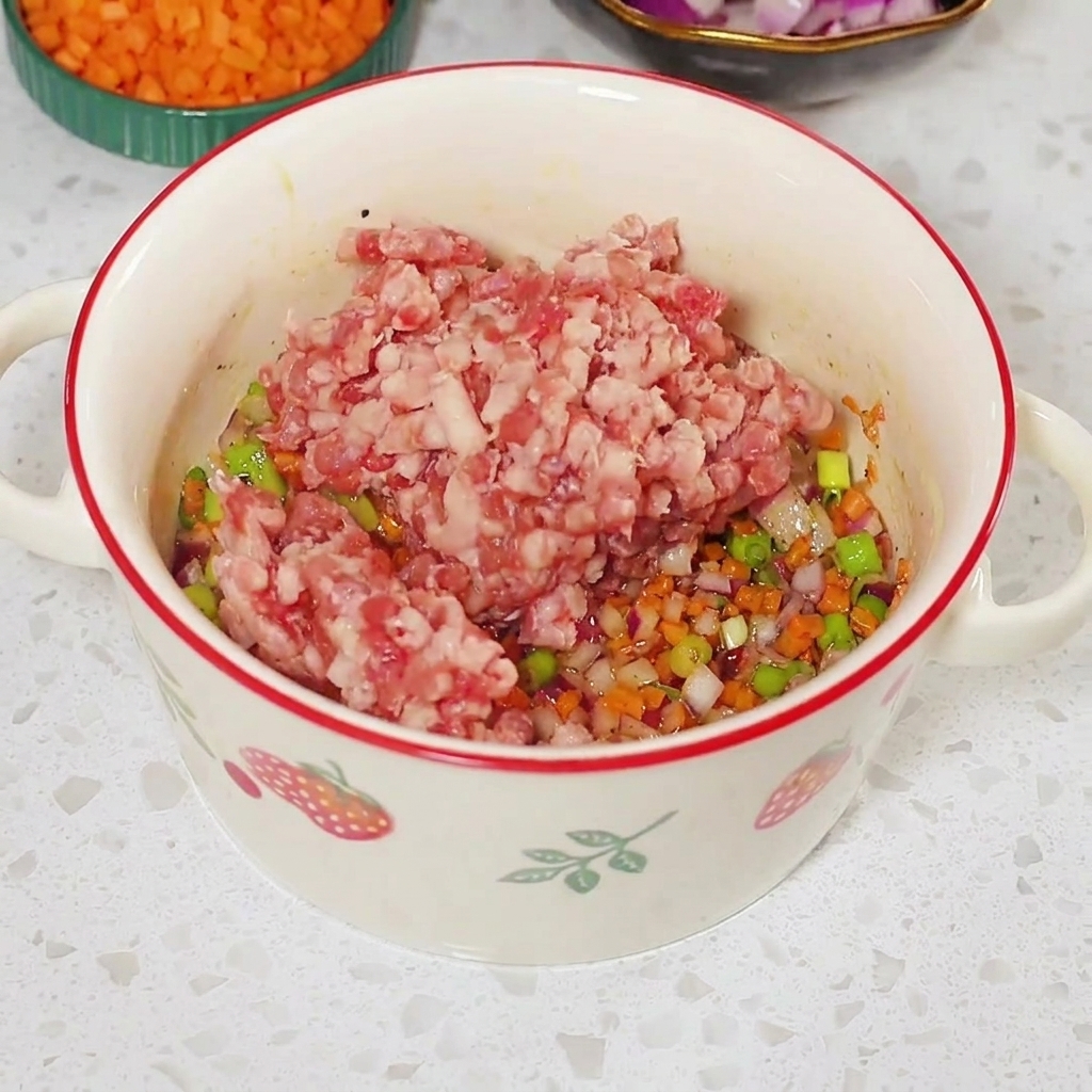 Carne picada cruda colocada encima de la mezcla de verduras sazonada dentro de un bol blanco.