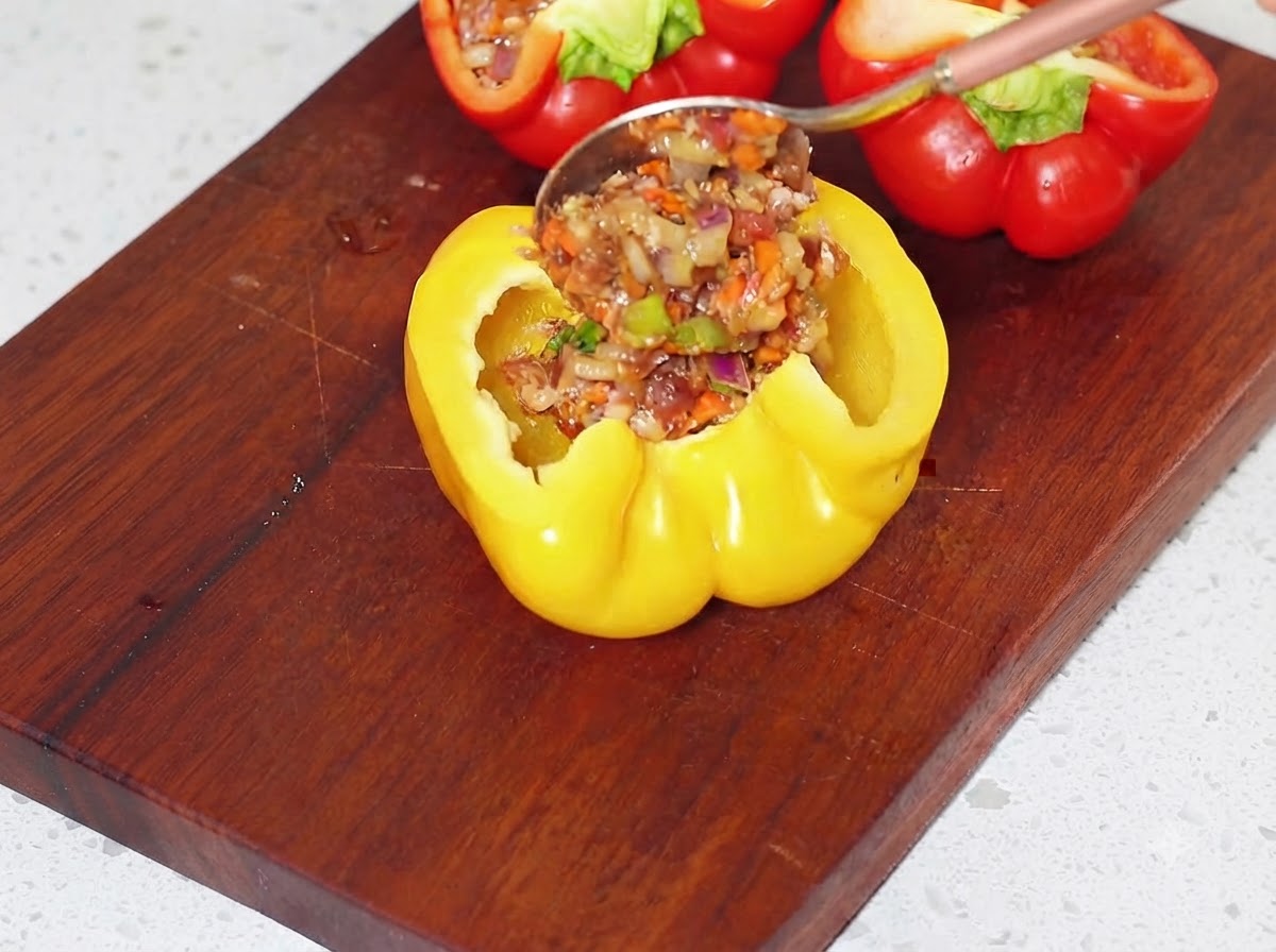 Rellenando con una cuchara las mitades de pimiento amarillo vacías con la mezcla de carne preparada en una tabla de cortar.