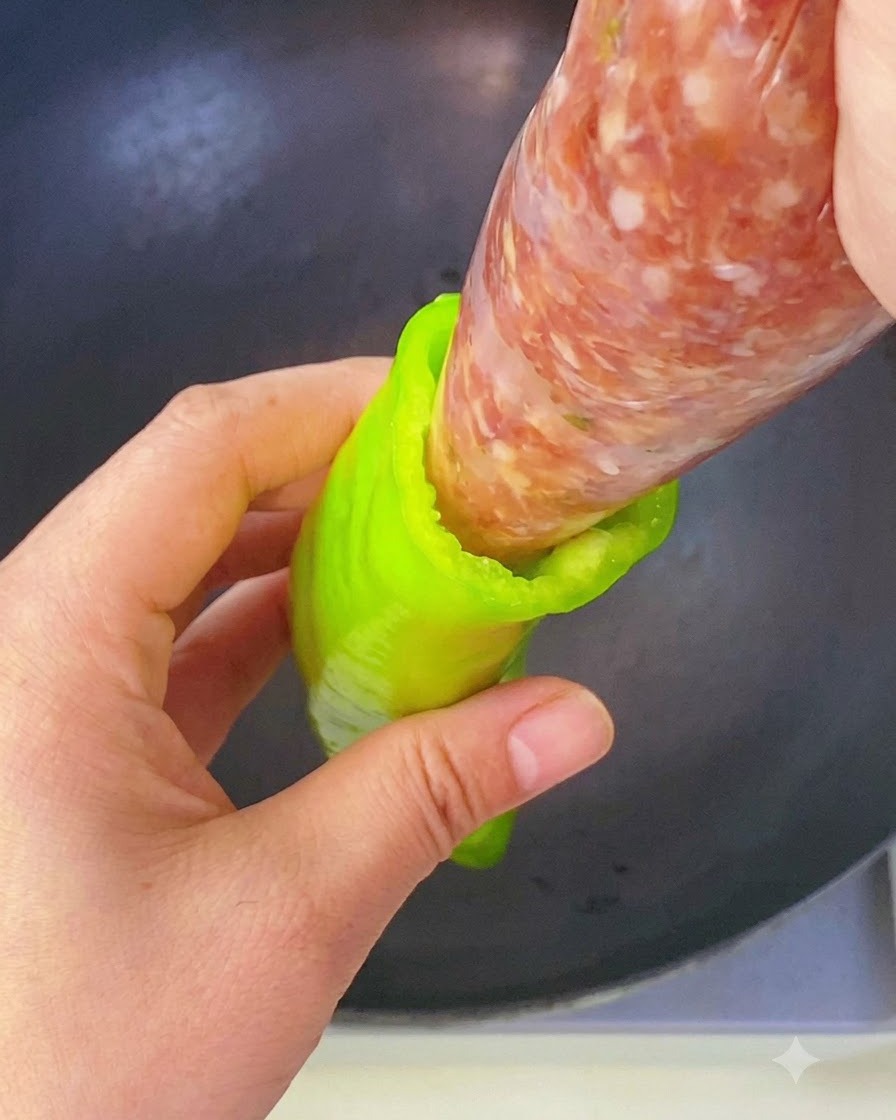 Una mano exprimiendo relleno de carne sazonada desde una manga pastelera directamente en la cavidad de un pimiento verde.