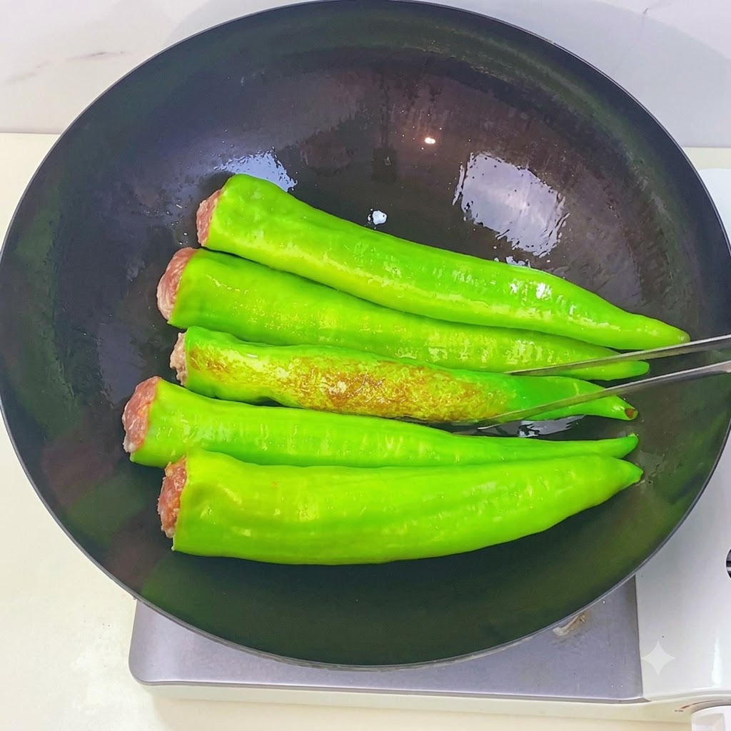 Pimientos verdes friéndose en un wok mostrando manchas tostadas tipo piel de tigre mientras se voltean con pinzas de cocina.