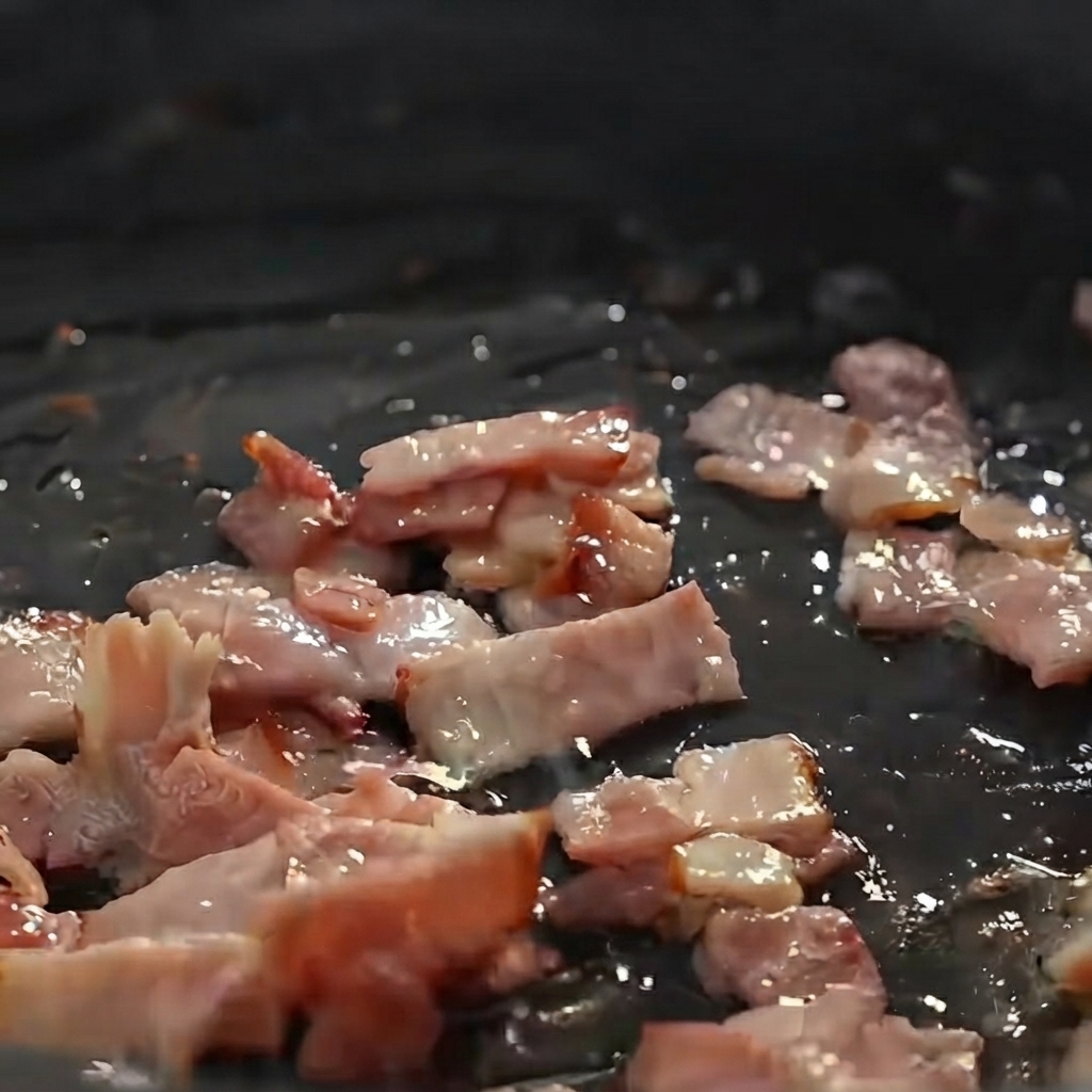 Papas, cebollas y apio en cubos siendo sofritos con trozos de tocino en una sartén.