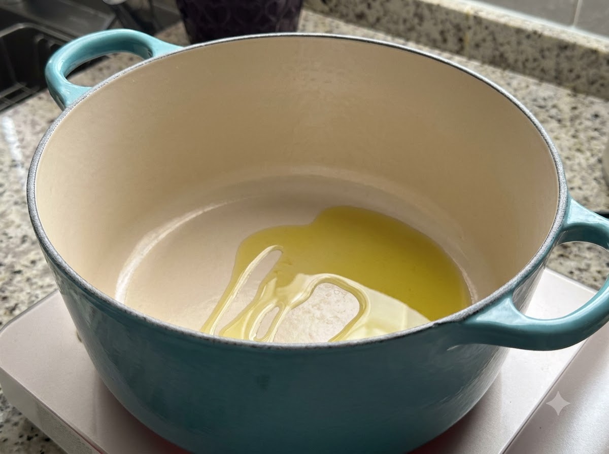 Una olla holandesa verde azulado sobre una estufa con un charco de aceite de oliva calentándose dentro.