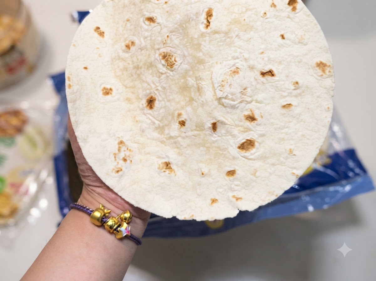 Primer plano de una mano sosteniendo una tortilla de harina redonda con manchas marrones características.