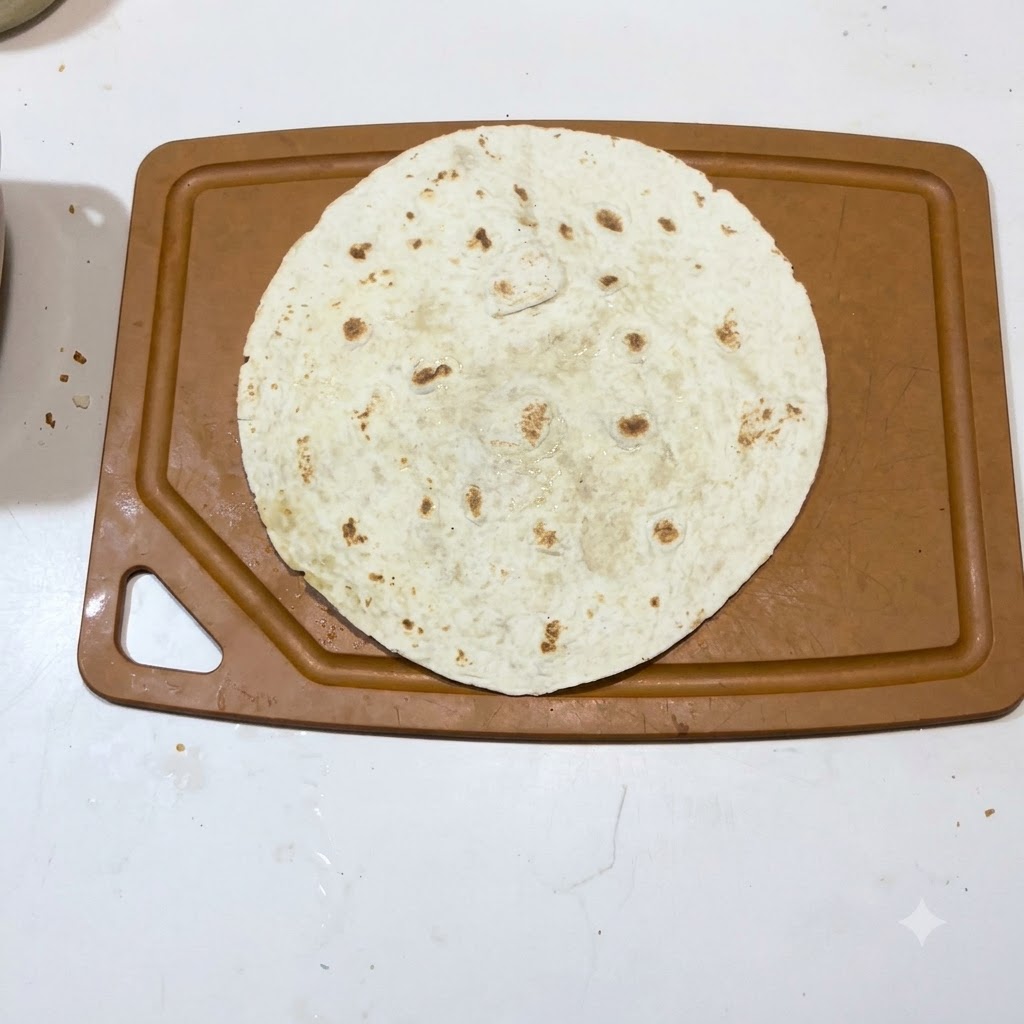 Una sola tortilla tibia colocada plana sobre la superficie de una tabla de cortar marrón.