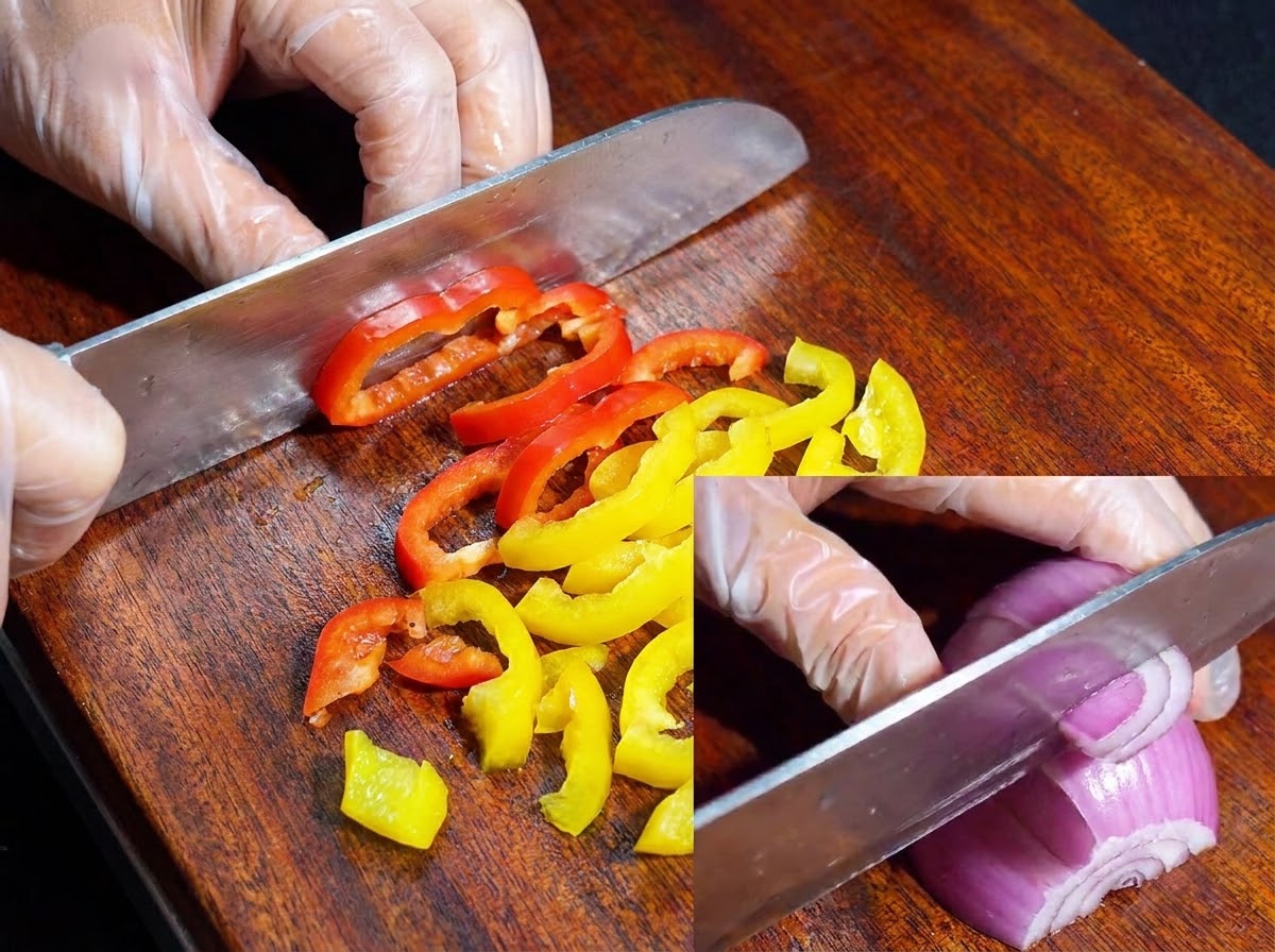 Un cuchillo cortando pimientos de colores y cebolla morada en una tabla de cortar de madera.