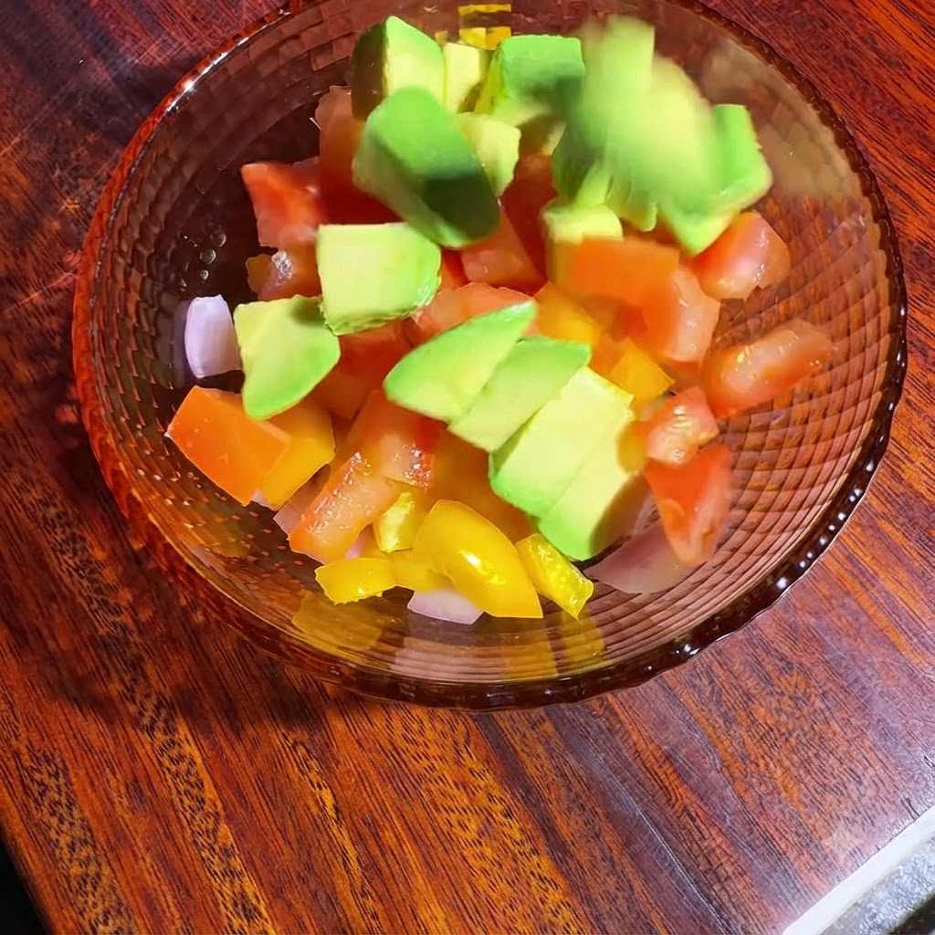 Un tazón de verduras picadas y aguacate siendo mezclado y sazonado con aceite y jugo de limón.