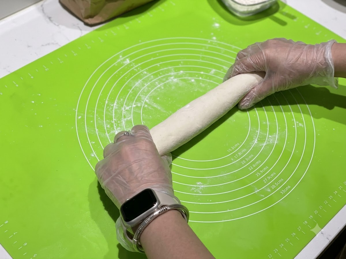 Manos enrollando un cilindro de masa sobre una estera de silicona verde con círculos de medición.