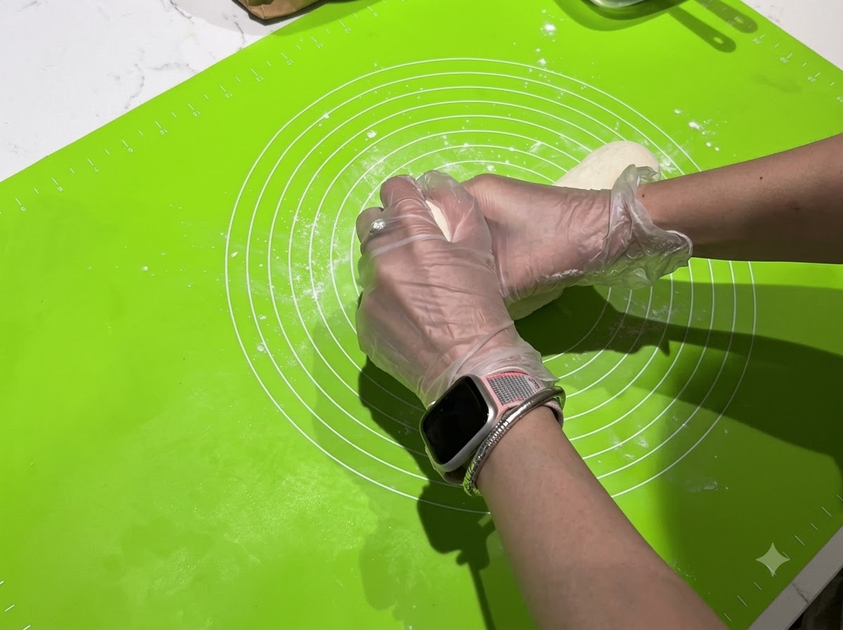 Manos dividiendo una tira larga de masa en porciones individuales más pequeñas sobre una estera verde.