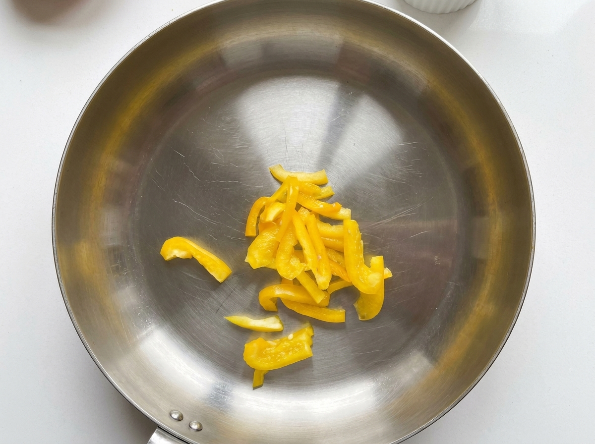 Pimientos amarillos cortados en rodajas en el centro de una sartén de acero inoxidable.