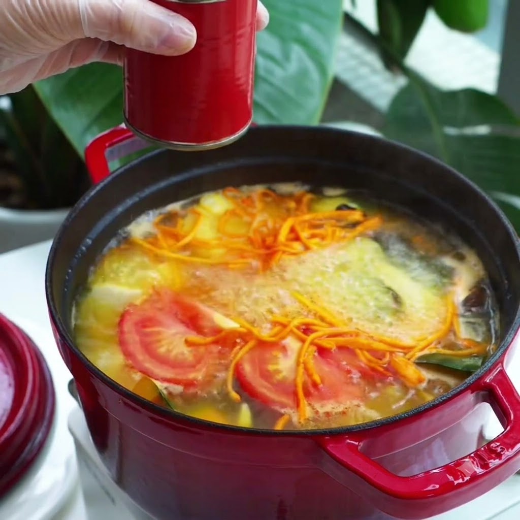 Una cucharada de condimento de pasta roja añadida a una olla de sopa de verduras hirviendo.