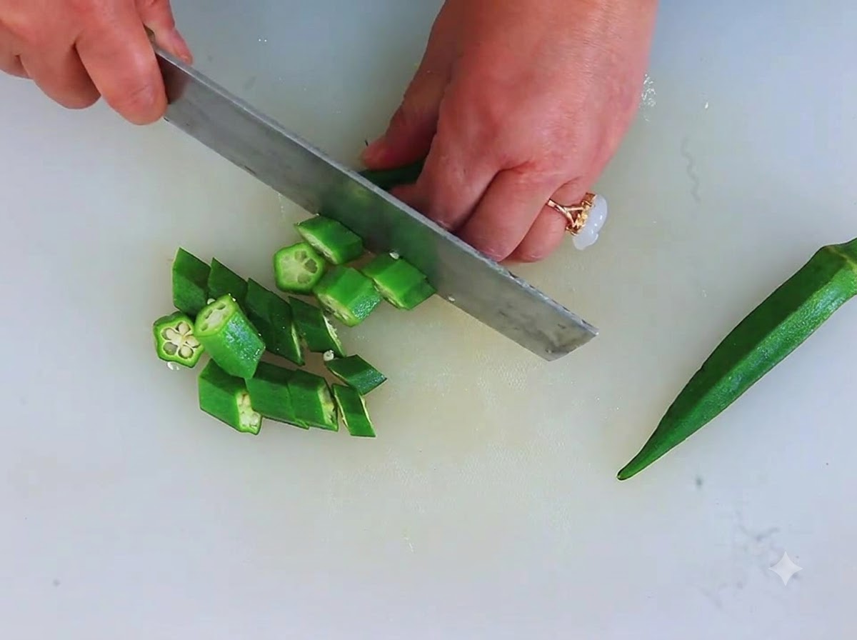 Okra verde fresca siendo picada en pequeñas piezas circulares en forma de estrella sobre una tabla de cortar.