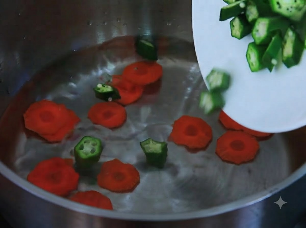 Zanahorias en rodajas y okra picada deslizándose desde un plato blanco hacia una olla llena de agua.