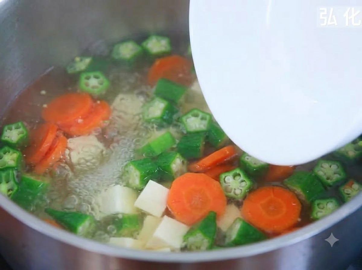 Cubos de tofu tierno siendo añadidos desde un plato a una olla hirviendo de sopa de verduras.