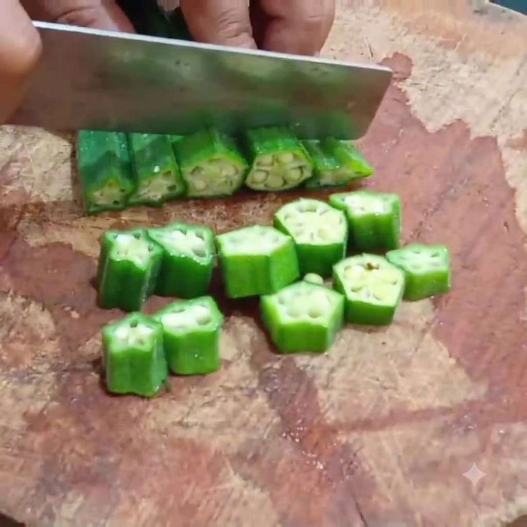 Un cuchillo de cocina cortando okra blanqueada en rodajas uniformes sobre una tabla de cortar de madera.