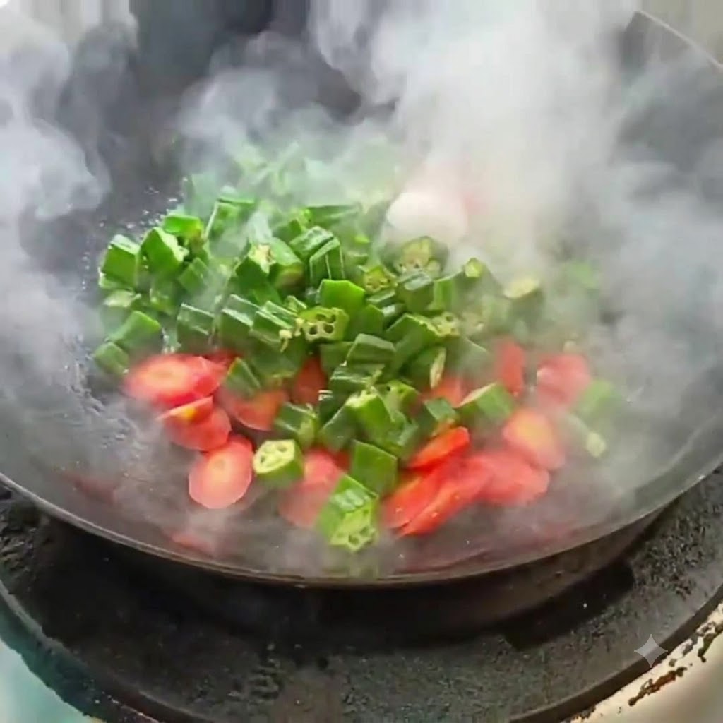 Okra en rodajas y zanahoria siendo salteadas en un wok caliente con vapor ascendente.