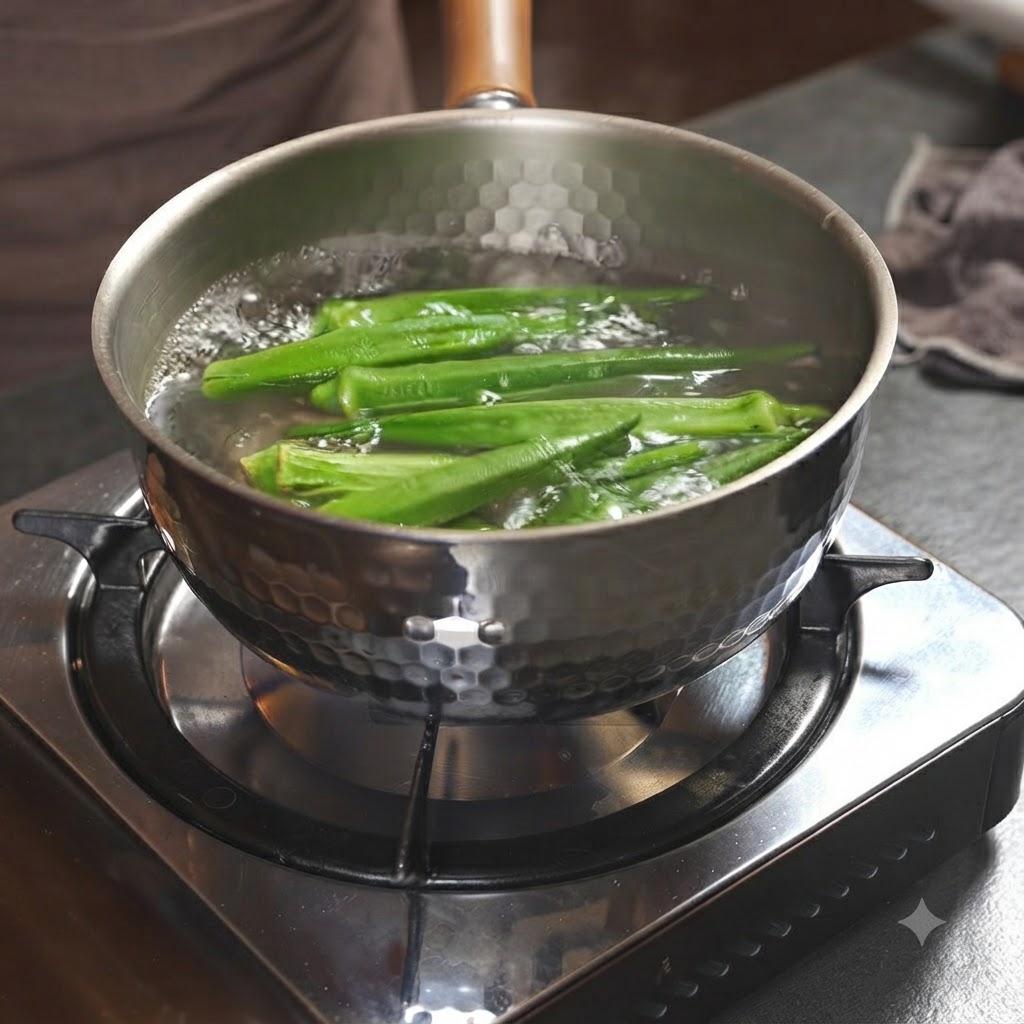 Vainas de okra verde hirviendo dentro de una olla metálica llena de agua en la estufa.