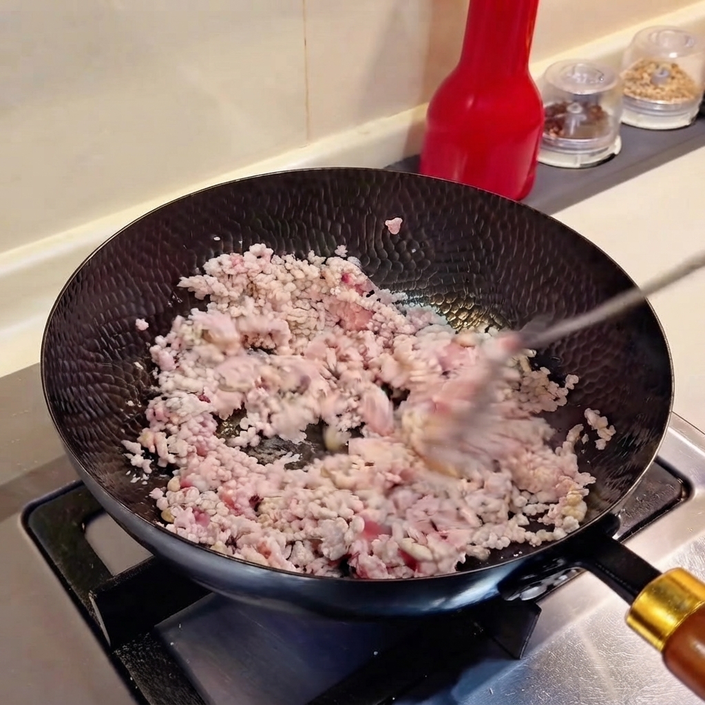 Cebolletas picadas y ajo picado siendo mezclados con carne picada en un wok.