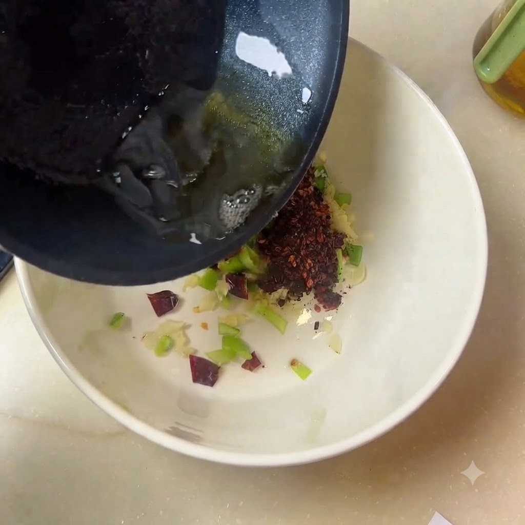 Aceite caliente cayendo desde una sartén hacia un bol blanco lleno de especias y aromáticos.